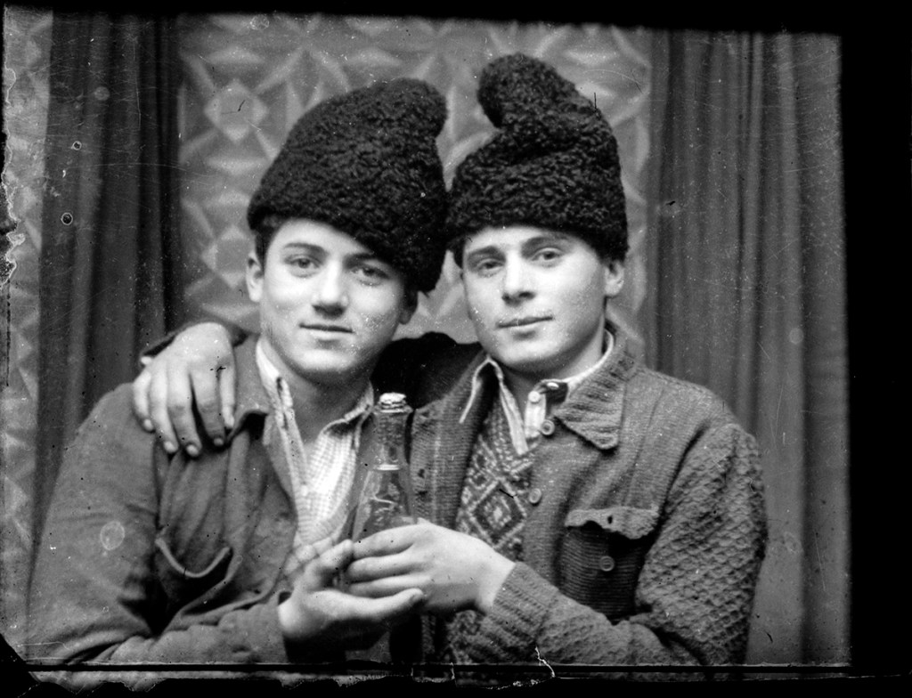 Two young romanian men in persian lambswool hats hold a bottle and gaze into the camera