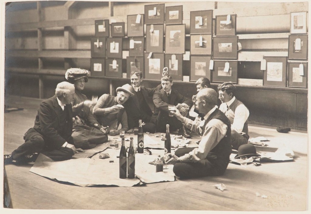 Society of Artists' Selection Committee, Sydney, 1907 showing seven men and one woman having an impromptu picnic in a large warehouse space