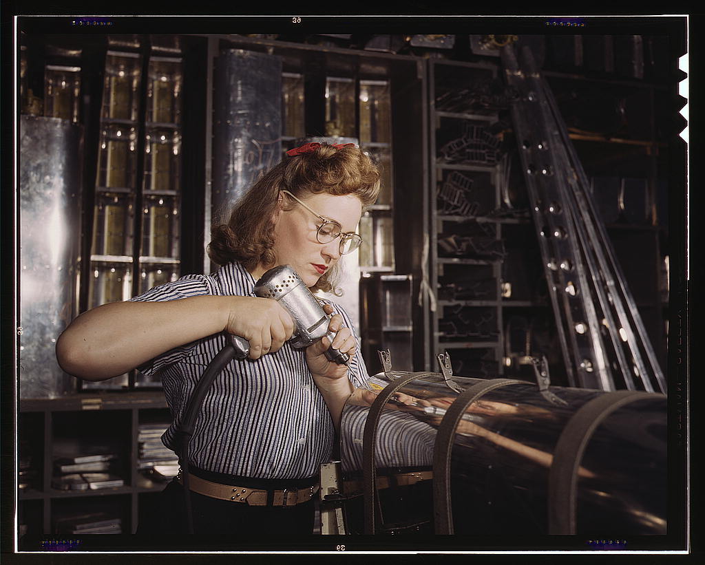 A woman operating a drill as she assembles part of an airplane