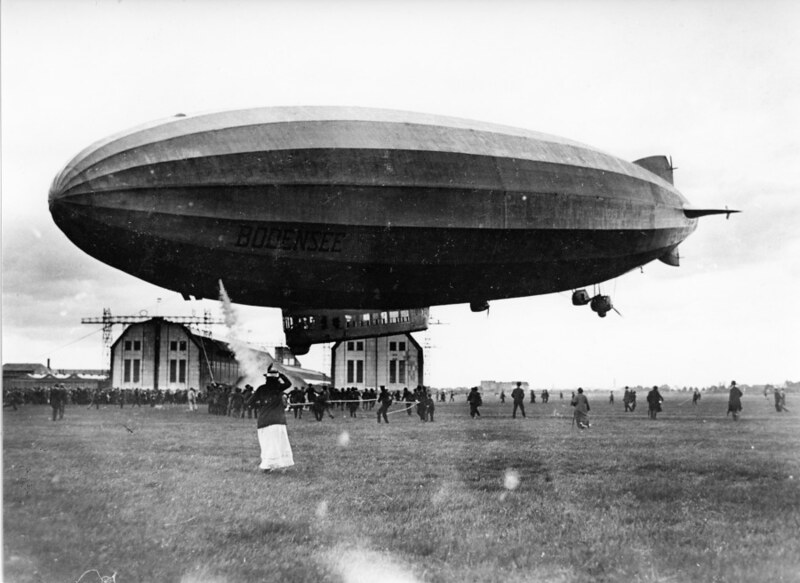 A small zeppelin hovering over two barns