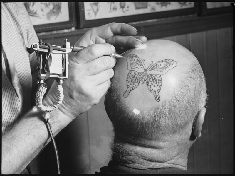 Photograph of a man getting his head tattooed with a butterfly