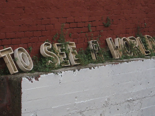 Letters spelling out TO SEE WORLD resting on a wall outside in front of a brick wall